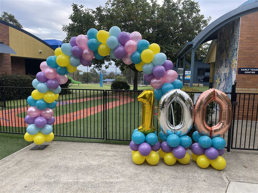 Pastel rainbow balloon arch beside a 100 number display