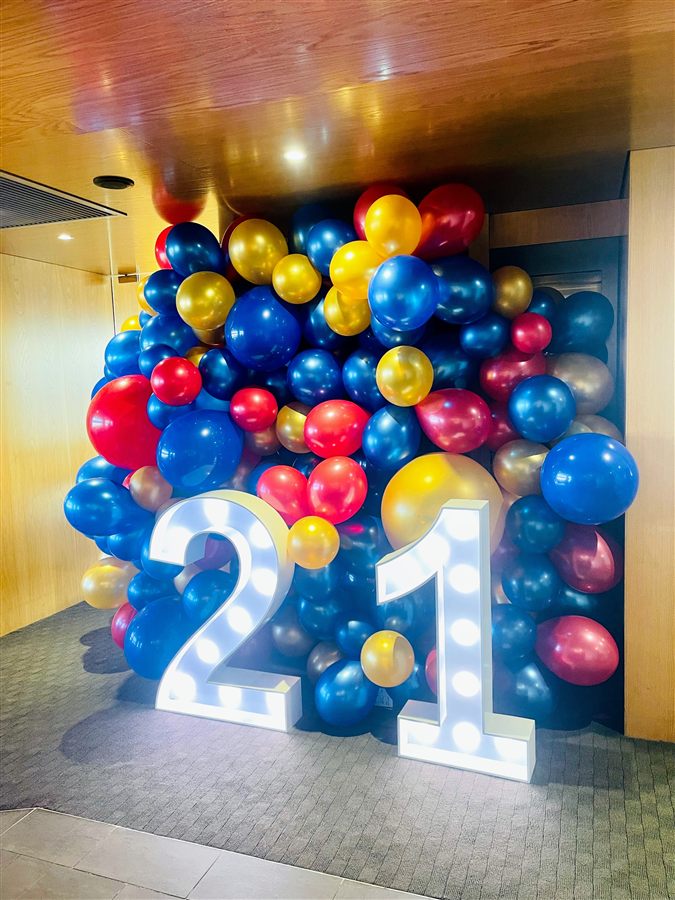 Blue, red and gold balloon wall with a light-up 21